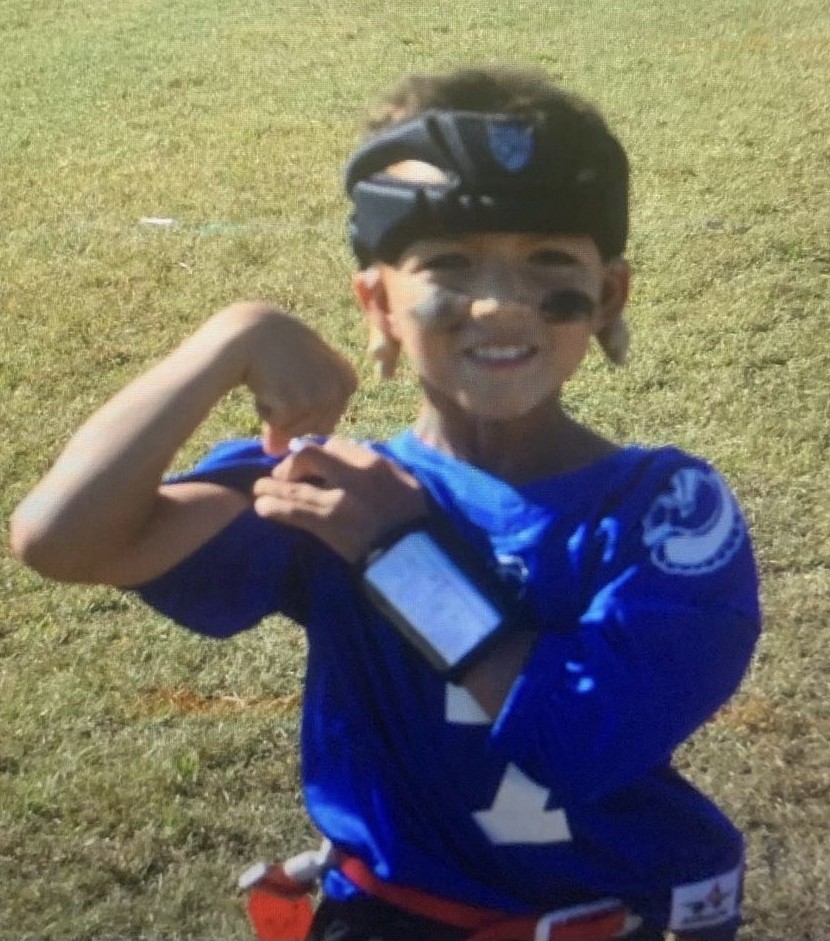 Randell as a young boy at flag football, flexing, wearing his cochlear implants