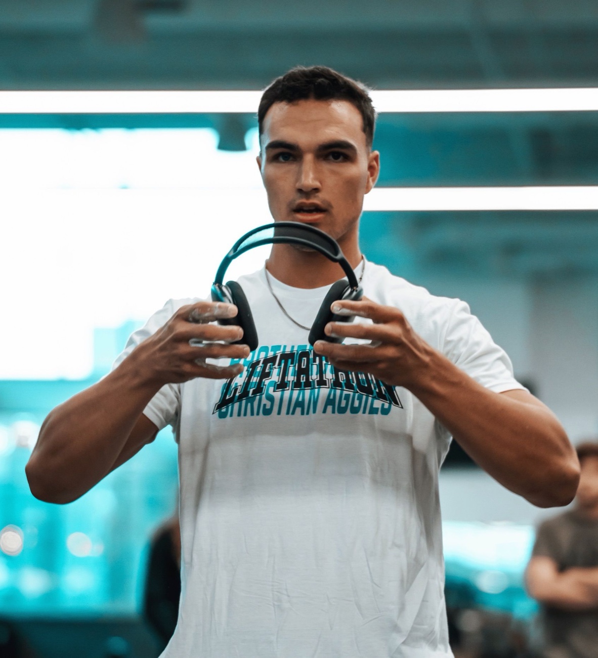 Randell in a Christian Aggies Liftathon shirt holding headphones in the gym